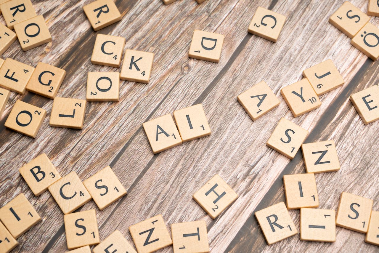 Wooden letter tiles scattered on a textured surface, spelling AI.